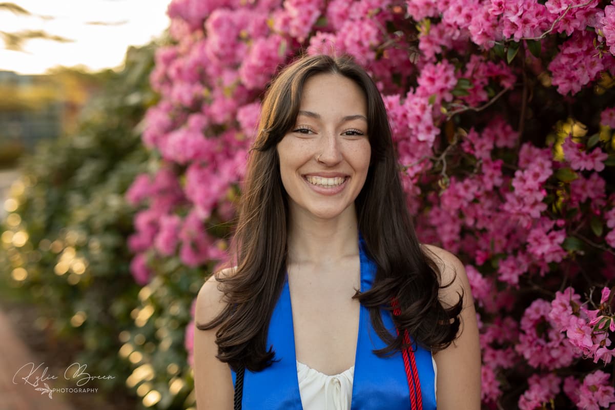 Emily Crain smiling in front of pink flowers after graduation